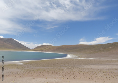 Sand dunes surrounding the lake under a blue but cloudy sky