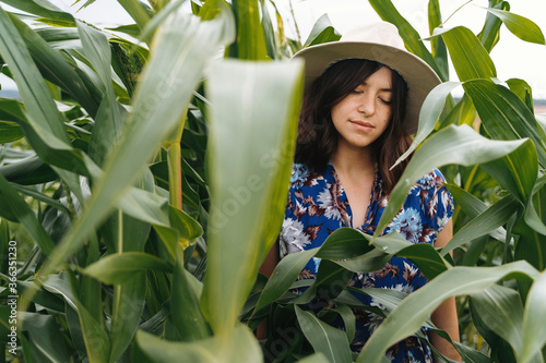 Fotografia Stylish young woman in blue vintage dress and hat posing in green corn field