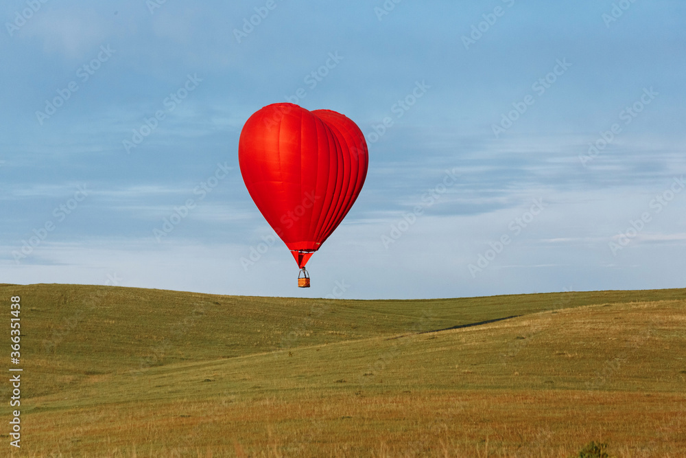 Fototapeta premium Hot air balloon in shape of heart is landing on the green field