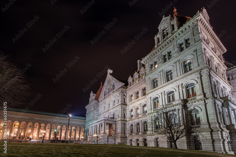 North entrance to granite and red roof New York State Capitol building at night with state Education Department building in the background.