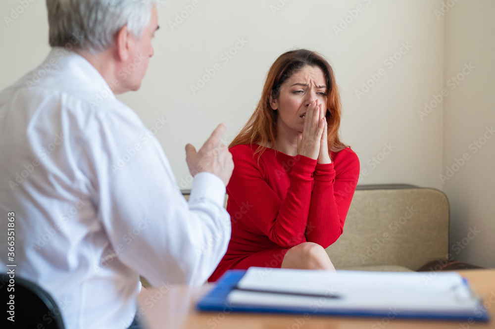 A frustrated crying woman holds her palms over face at a session with a male psychologist. Mature psychotherapist talking to a female patient with depression and neurosis. Mental health treatment. A frustrated crying woman holds her palms over face at a session with a male psychologist. Mature psychotherapist talking to a female patient with depression and neurosis. Mental health treatment.