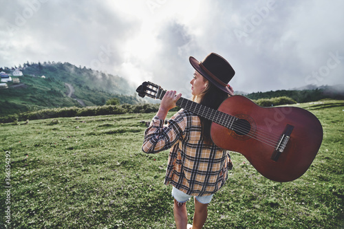 Young free hipster woman traveler with guitar while traveling to the mountains. Country music