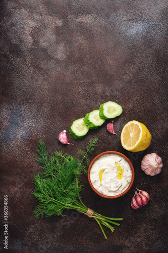 Traditional greek tzatziki sauce with ingredients on dark rustic background. Greek yogurt with cucumber, dill, garlic and lemon. Top view, copy space, flat lay