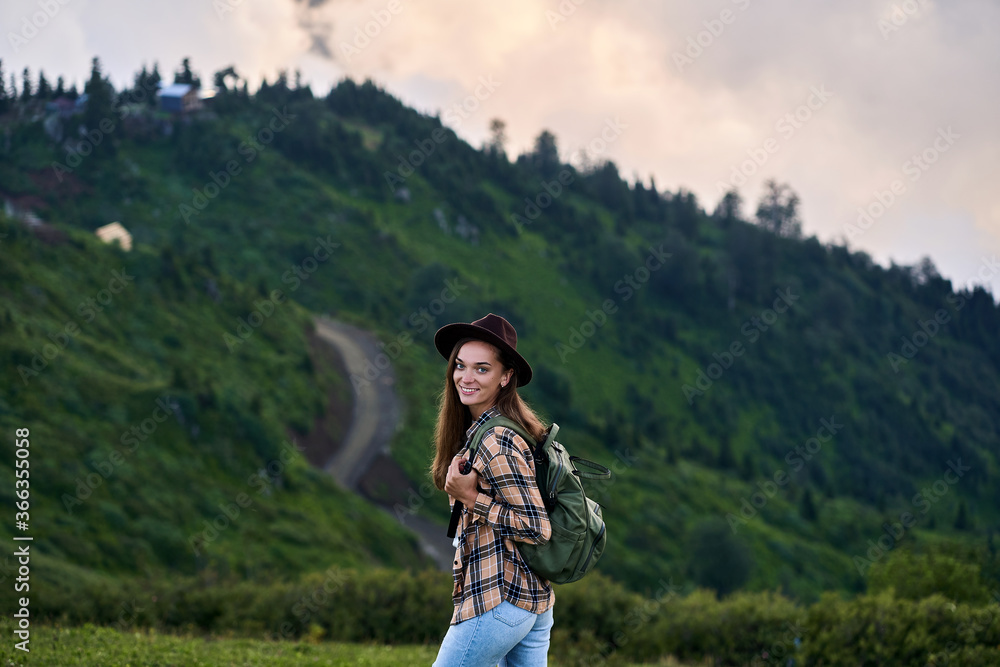 Portrait of free happy smiling joyful backpacker woman tourist wearing hat during adventure trip in the green high mountains
