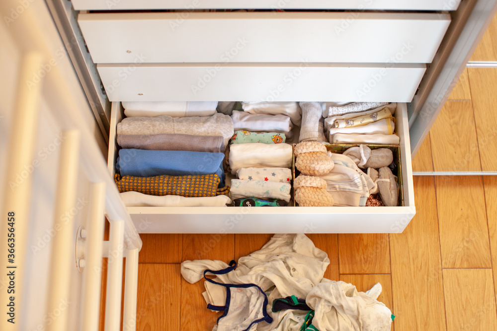 Vertical storage of clothing. A pregnant girl is preparing for the birth of a child. She takes apart the clothes. Room interior. Neatly folded clothes in chest of drawers. Newborn baby clothes. 