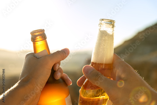 Close up cropped female and male hands holding and clanging beer glass bottles outdoor