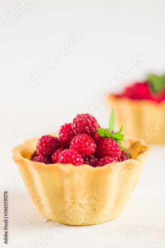Homemade shortcrust raspberry pastry. Summer berries mini tartlets with vanilla custard and mint leaves. Fresh desserts on the white background isolated. Free copy space.