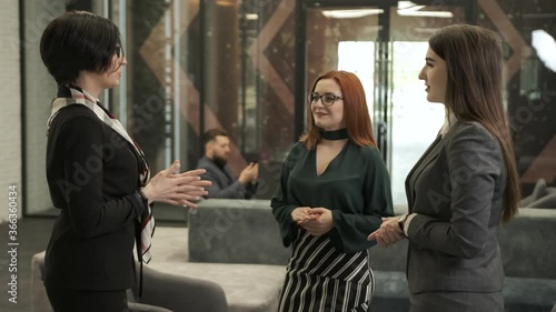 Three business women are standing inside the business building and talk about new project and things to do next. 