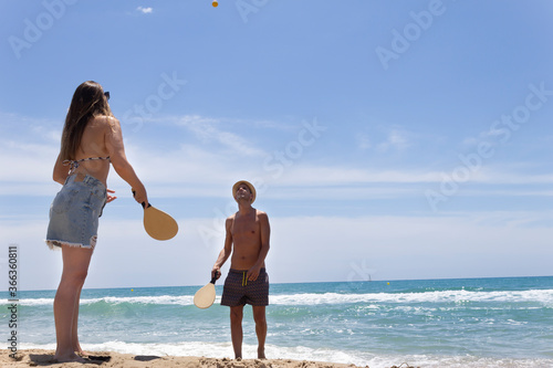 Young beautiful couple playing paddle ball on the beach in summer (tennis).Happy Holidays  concept lifestyle.