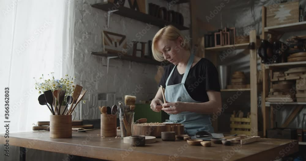 Woman carpenter polishes wooden spoon with a sandpaper Woman carpenter polishes wooden spoon with a sandpaper