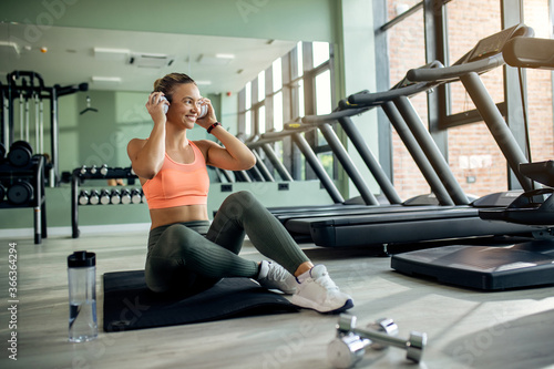 Happy athletic woman listening music on headphones in a gym.