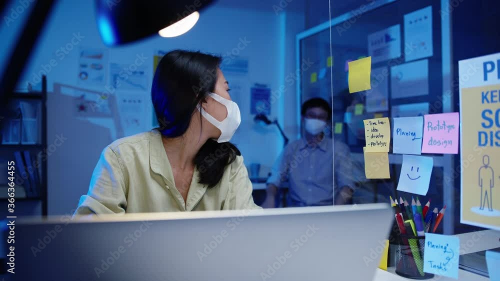 Asian businessman turn off computer and say goodbye his colleague who still working when he get off work after finish working overtime in small modern home office night. Coworker partnership concept. Asian businessman turn off computer and say goodbye his colleague who still working when he get off work after finish working overtime in small modern home office night. Coworker partnership concept.