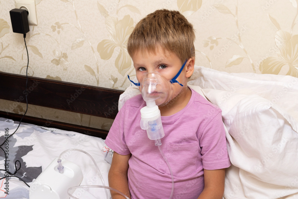 The boy inhales the medicine with a nebulizer and oxygen mask The boy inhales the medicine with a nebulizer and oxygen mask