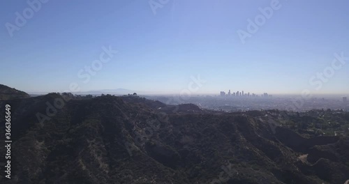 Aerial of Hollywood Hills with Los Angeles Observatory shown on Mountain Top, Downtown Skyscrapers shown in Horizon and Blue Sunny Sky