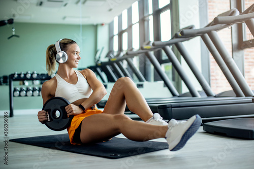 Young female athlete doing abdominal exercises with weight plate at health club.
