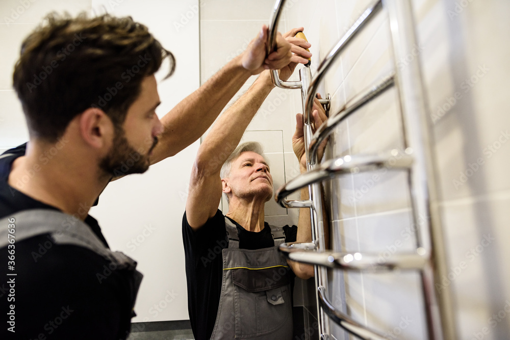 Two plumbers, workers in uniform working, installing towel rail