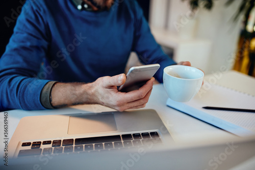 Closeup of freelancer using smart phone on coffee break in his home office.