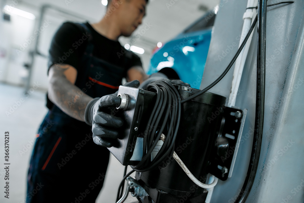 Fototapeta premium Close up of hand of professional male mechanic operating hydraulic lift, pushing button up at auto repair shop