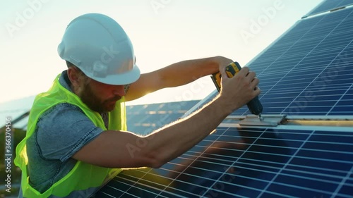 At sunlight man worker fixing solar panel to a metal basis with a drill in a sunny day green environmental rooftop construction engineer photovoltaic electricity battery utility slow motion photo