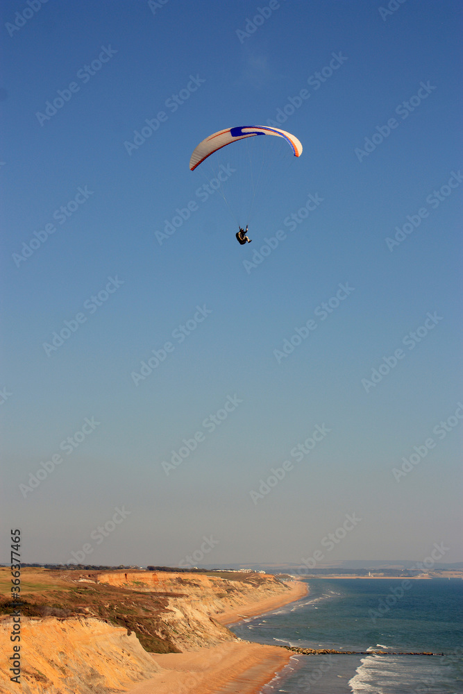 man is flying on white paraglider in the sky above the blue sea.. English canal, Barton-on-sea, England man is flying on white paraglider in the sky above the blue sea.. English canal, Barton-on-sea, England