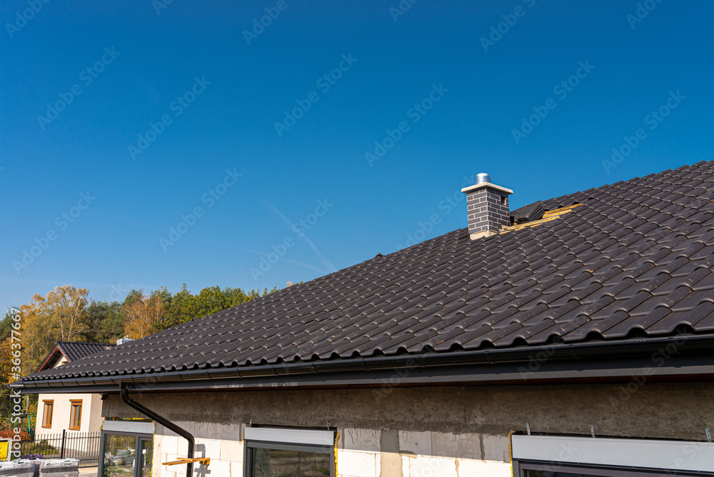 The roof of a single-family house covered with a new ceramic tile in anthracite, against the blue sky. The roof of a single-family house covered with a new ceramic tile in anthracite, against the blue sky.