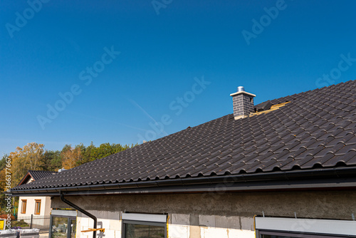 The roof of a single-family house covered with a new ceramic tile in anthracite, against the blue sky.