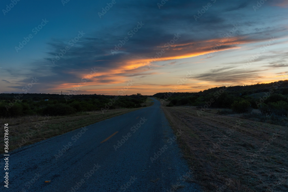 Band of gray and orange clouds glowing over rural country road Band of gray and orange clouds glowing over rural country road