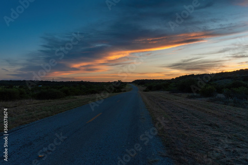 Band of gray and orange clouds glowing over rural country road © Stretch Clendennen