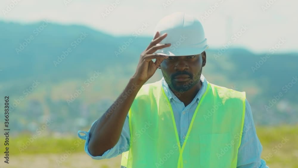Portrait of african american young man stand look at camera puts on a helmet engineers in special uniform field at sunlight technology modern electricity energy slow motion Portrait of african american young man stand look at camera puts on a helmet engineers in special uniform field at sunlight technology modern electricity energy slow motion