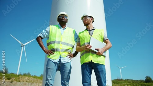 Two workers men in uniform discuss the wind turbines stand ecological energy industry power windmill field worker renewable slow motion