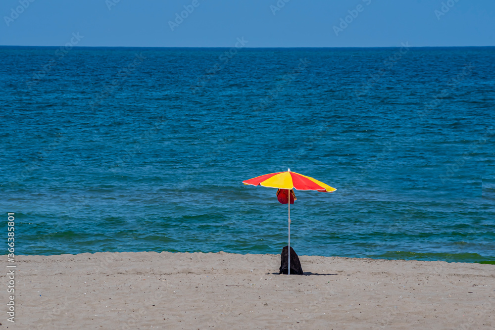A yellow red beach umbrella and a backpack on the beach