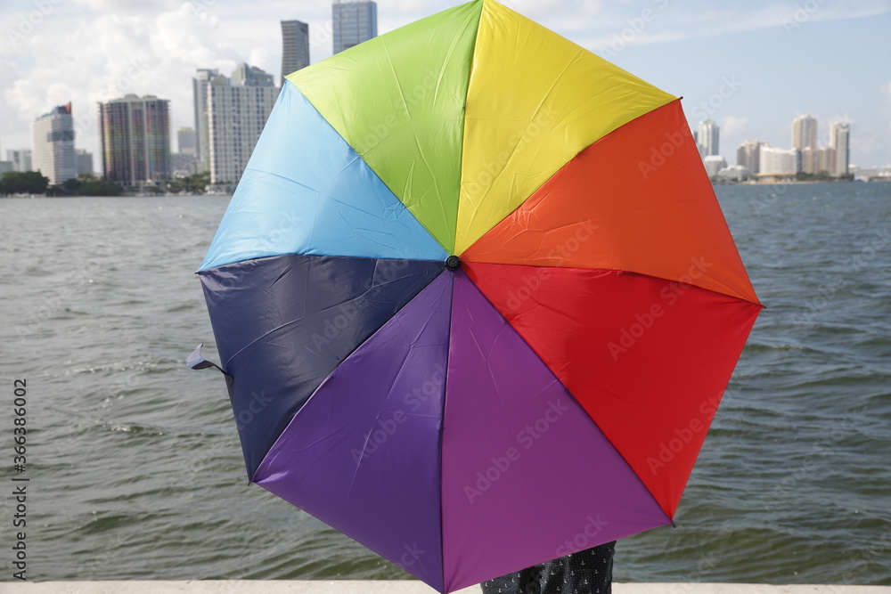 colorful umbrella of rainbow colors on the background of city skyscrapers and water of the river or sea. LGBT pride concept