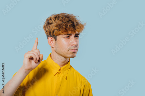 seriously boy pointing fingers up, at copy space, isolated over blue background, teenager cu coafura la moda, handsome guy in camasa galbena, tip tanar, nice teenager, photo