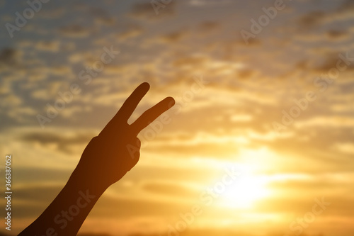 Silhouette of hand showing two fingers up over sunset background.