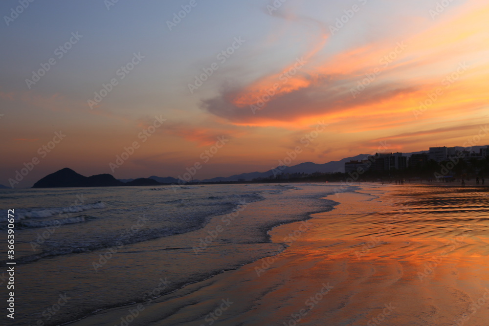 Ocean with calm waves on the shore during a beautiful red sunset. Bertioga, city, Brazil