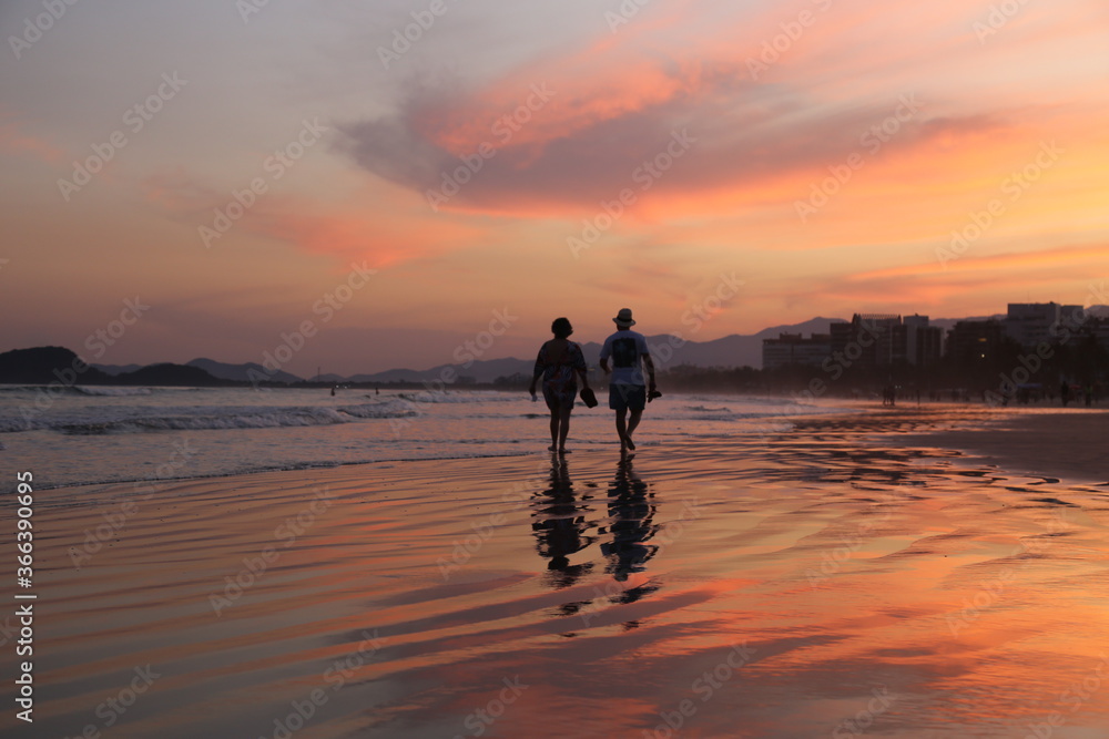 Couple walking on the beach during a beautiful red sunset. Bertioga, city, Brazil