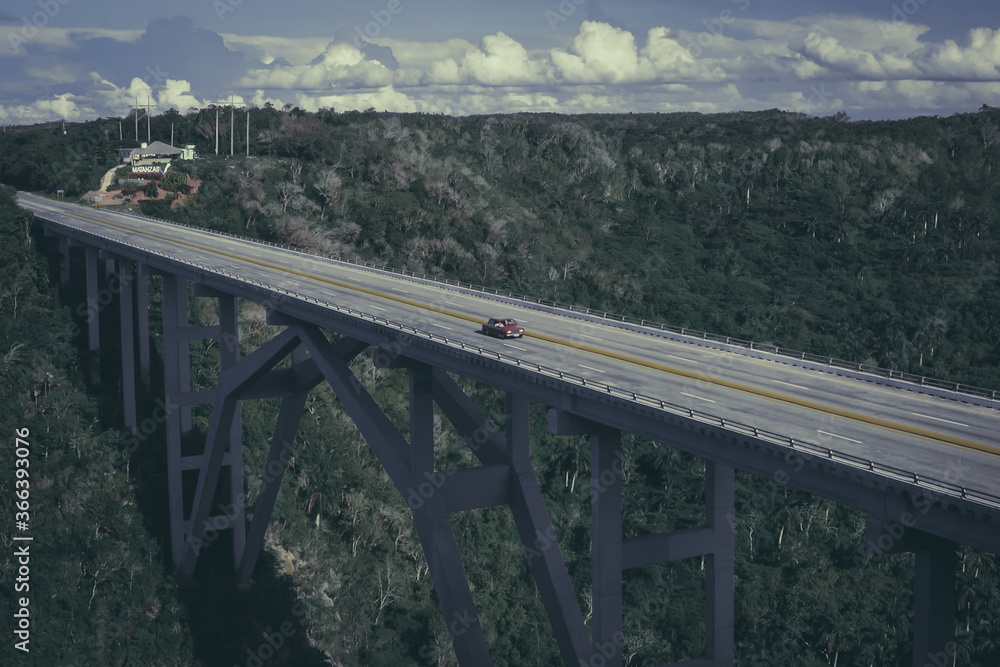 Vehículo antiguo cruza el puente sobre el bosque. Puente de autopista con un vehículo rojo solitario. Cuba. Vehículo antiguo cruza el puente sobre el bosque. Puente de autopista con un vehículo rojo solitario. Cuba.