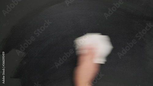 woman's hand wipes a black chalk board with a white rag, close up