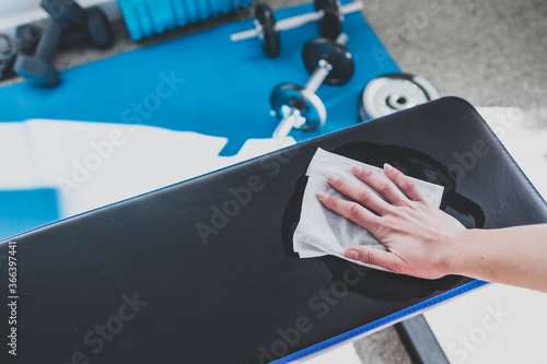 Fototapeta the new normal after covid-19, hand cleaning gym equipment with disinfectant wip