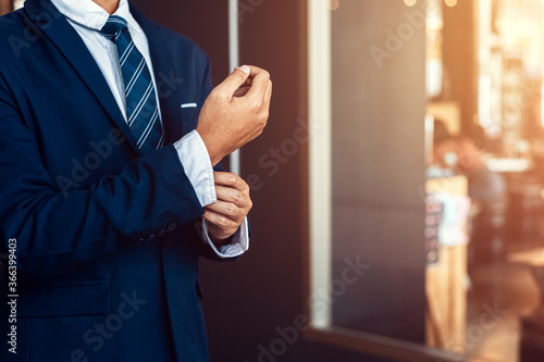 businessman wearing business suit fasten cufflink or button on sleeve of classic jacket and factory background.