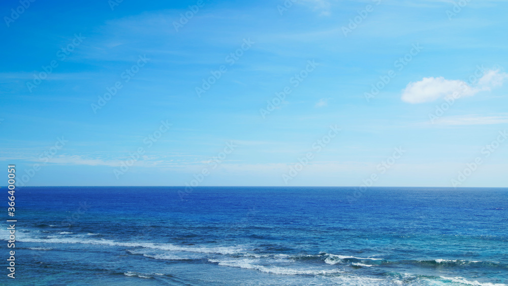 Horizon seascape with blue sky, waves on the water of a sandy beach