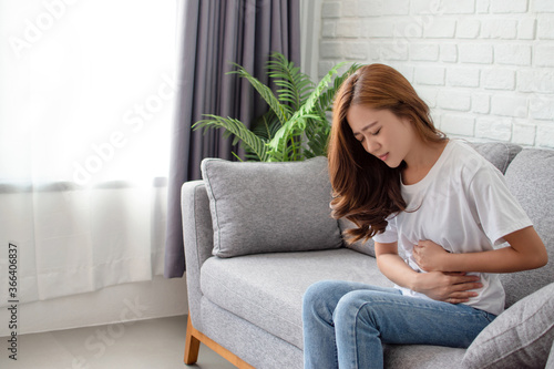 Asian women have stomach pain or menstruation. She sat on the sofa in the living room.