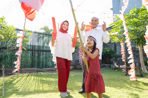 grandfather, grandmother, and grandchildren wear red and white clothes and attributes to commemorate Indonesia's independence day