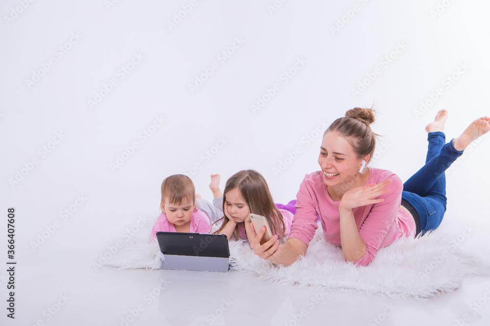 Modern technologies in everyday life: woman talks on phone through headset, children watch cartoon on tablet. Hobbies and recreation with gadgets. Family vacation. Parents with girls on floor Modern technologies in everyday life: woman talks on phone through headset, children watch cartoon on tablet. Hobbies and recreation with gadgets. Family vacation. Parents with girls on floor