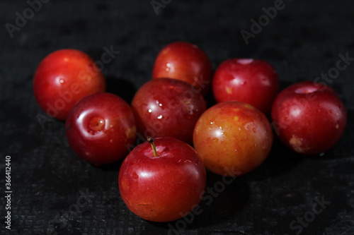 Closeup of fresh red juicy plums with droplets of water on a black background. Closeup shot of Satsuma red plums