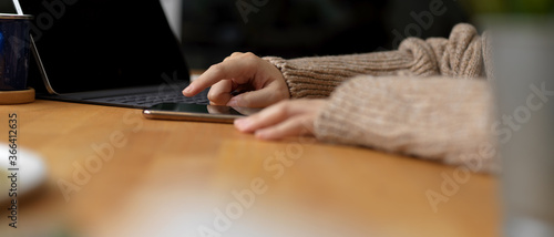Female touching on smartphone while sitting at workspace with digital tablet and copy space on wooden table