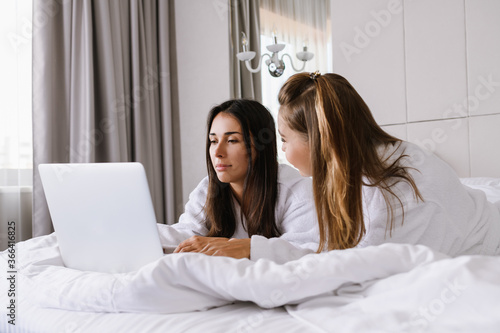 Two concentrated women in bed with laptop