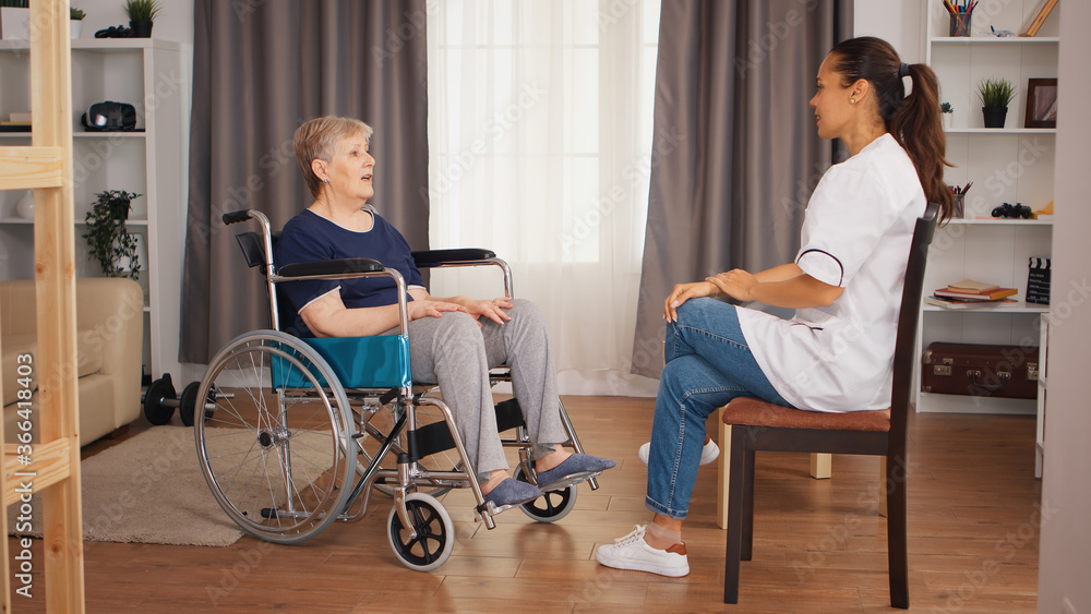 Handicapped senior woman in wheelchair talking with female nurse. Old person retirement home, healthcare nursing, health support, social assistance, doctor and home service Handicapped senior woman in wheelchair talking with female nurse. Old person retirement home, healthcare nursing, health support, social assistance, doctor and home service