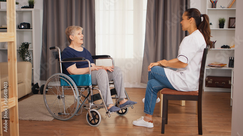 Handicapped senior woman in wheelchair talking with female nurse. Old person retirement home, healthcare nursing, health support, social assistance, doctor and home service