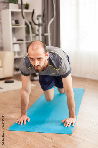 Fit man in his apartment doing mountain climbers exercise on yoga mat during global pandemic.